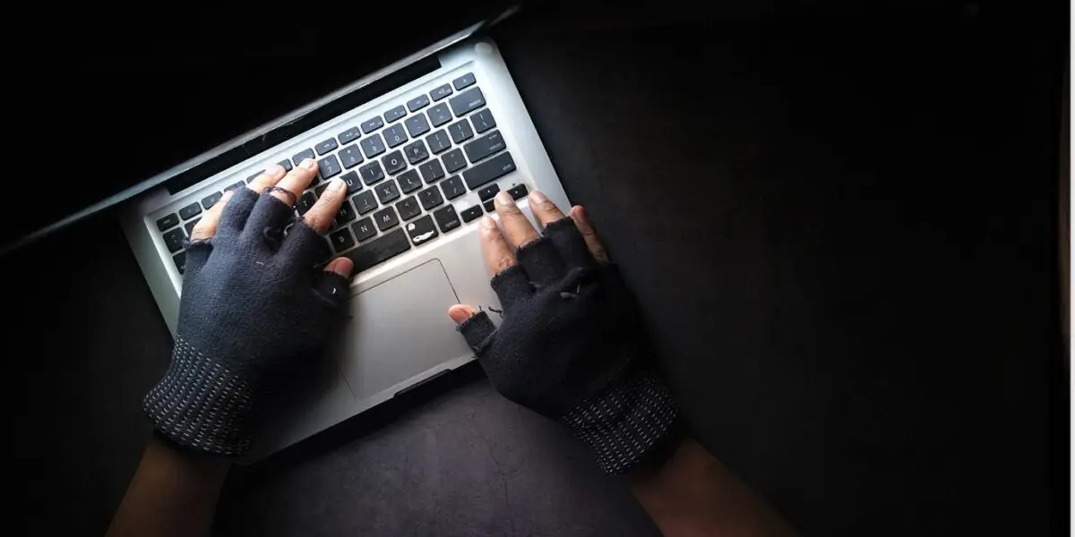Illustration of a man wearing gloves typing on a computer in a dark setting.